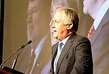 Malcolm Turnbull speaking in the Great Hall of Parliament House with a projection screen behind him showing three other people.